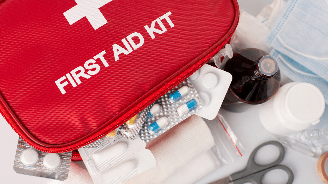 A workplace first aid kit placed on a desk, surrounded by safety equipment like gloves and bandages, symbolising readiness for emergencies.
